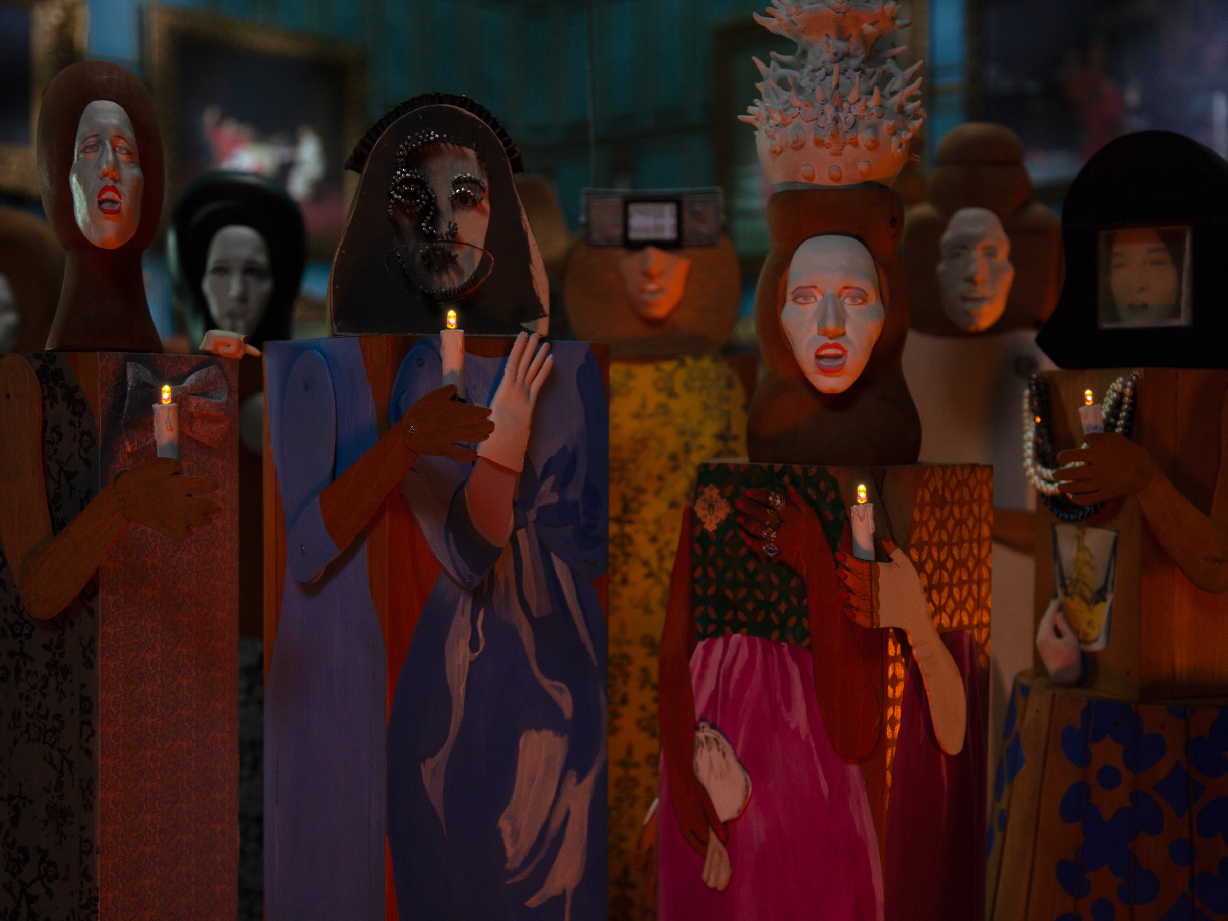 Stop-motion still: a crowd of masked puppet figures in patterned robes holding candles