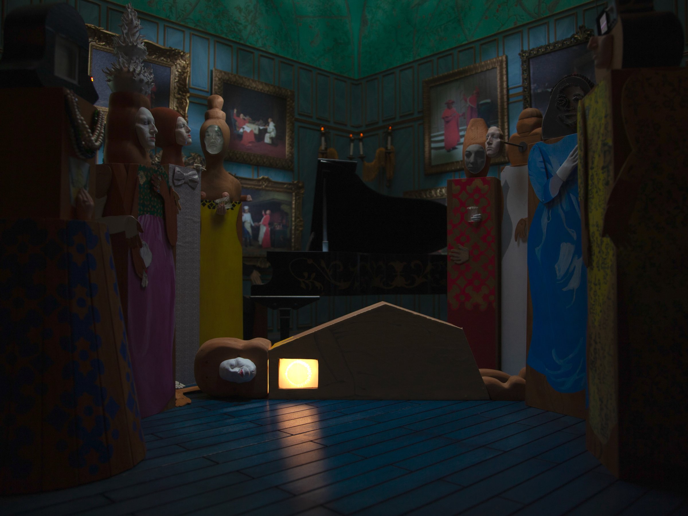 Stop-motion still: masked puppet figures lining the walls of a dark parlor around a small glowing house