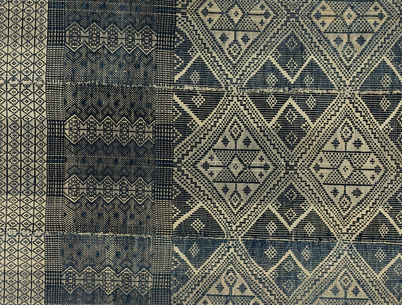 Detail from a piece of blue and white woven cloth, the left is plaid with dark blue vertical lines, and the right side has intricate diamond patterns.