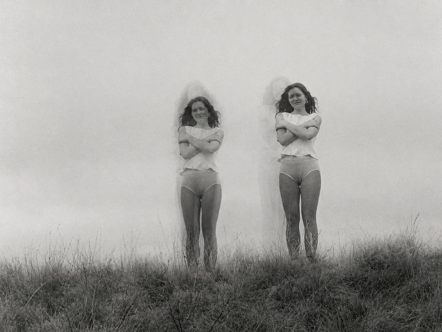 Black-and-white photograph of two young women with arms crossed standing in a grassy field