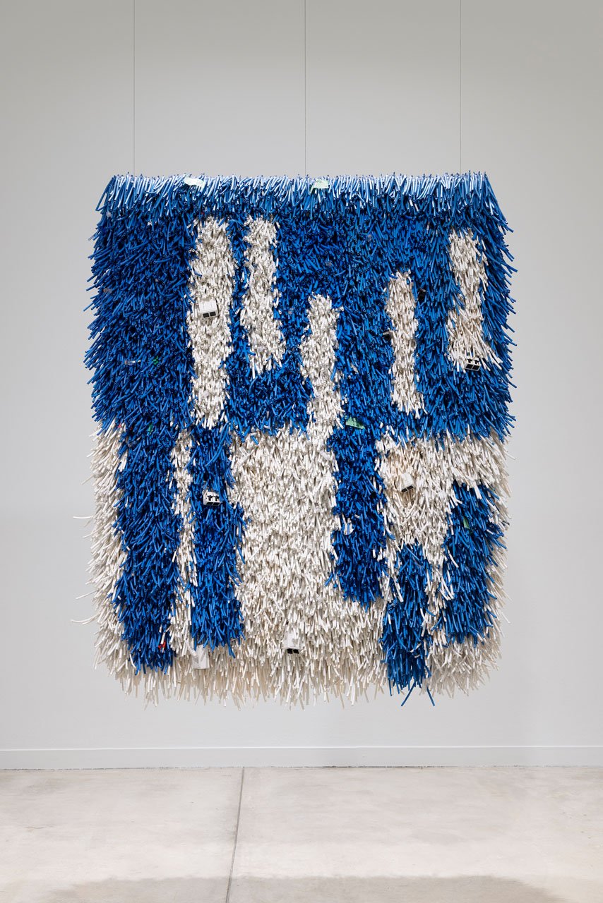 Emily Hermant’s Pile It On, a hanging of blue and white folded ethernet jackets