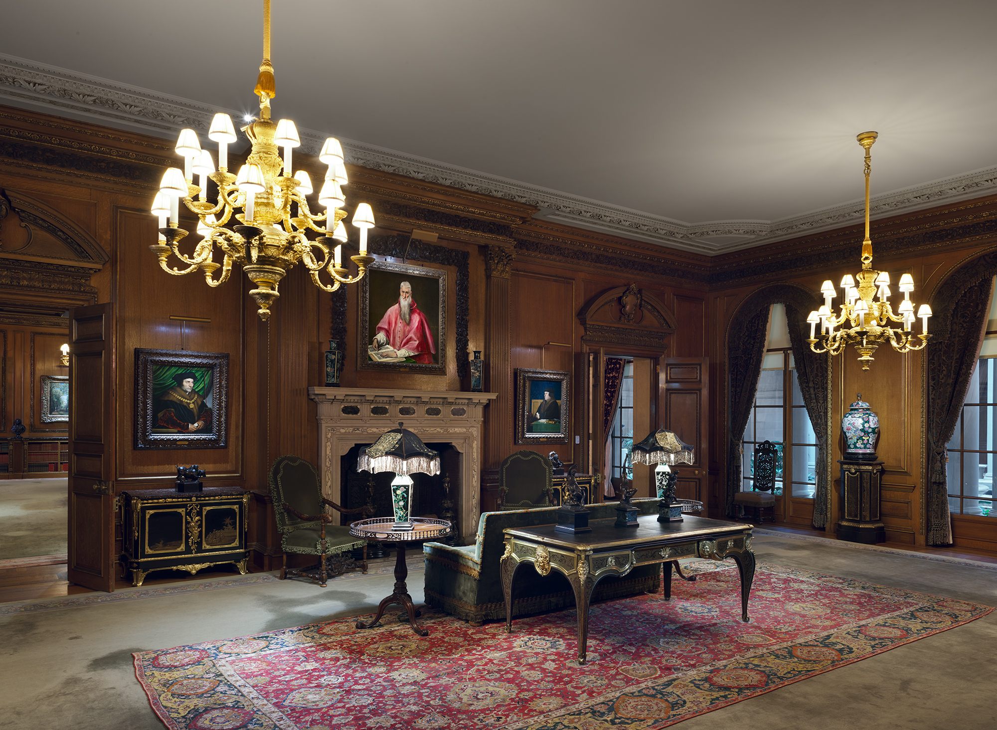 The Living Hall: a wood-panelled room with chandeliers, paintings on every wall, a desk and a patterned rug.