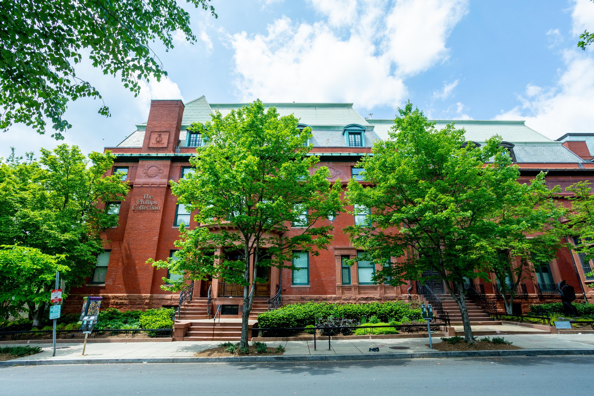 Frontal view of The Phillips Collection's historic Duncan Phillips house, a four-storey red brick terrace behind a row of street trees