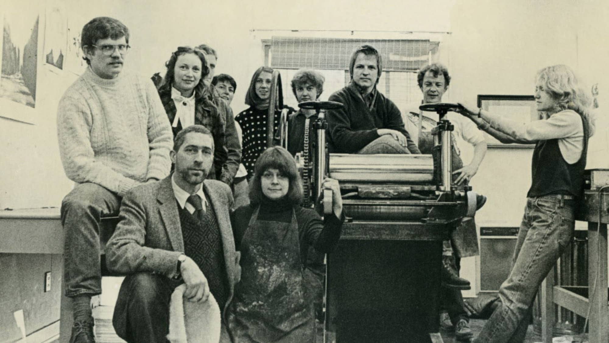 A group of people sitting and standing around printing equipment.