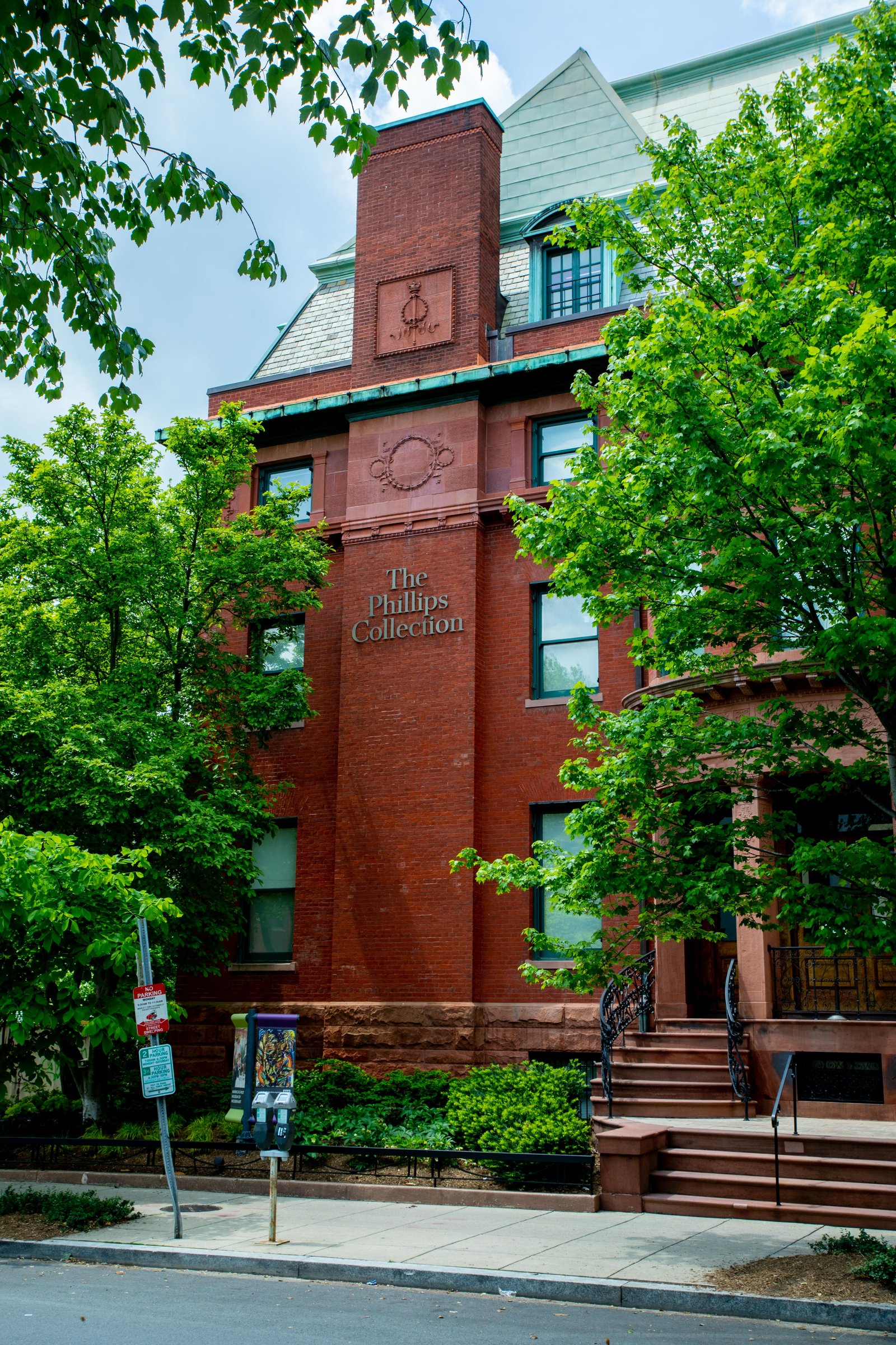 Tall red-brick corner of the Phillips Collection with a stone sign, steps and summer trees