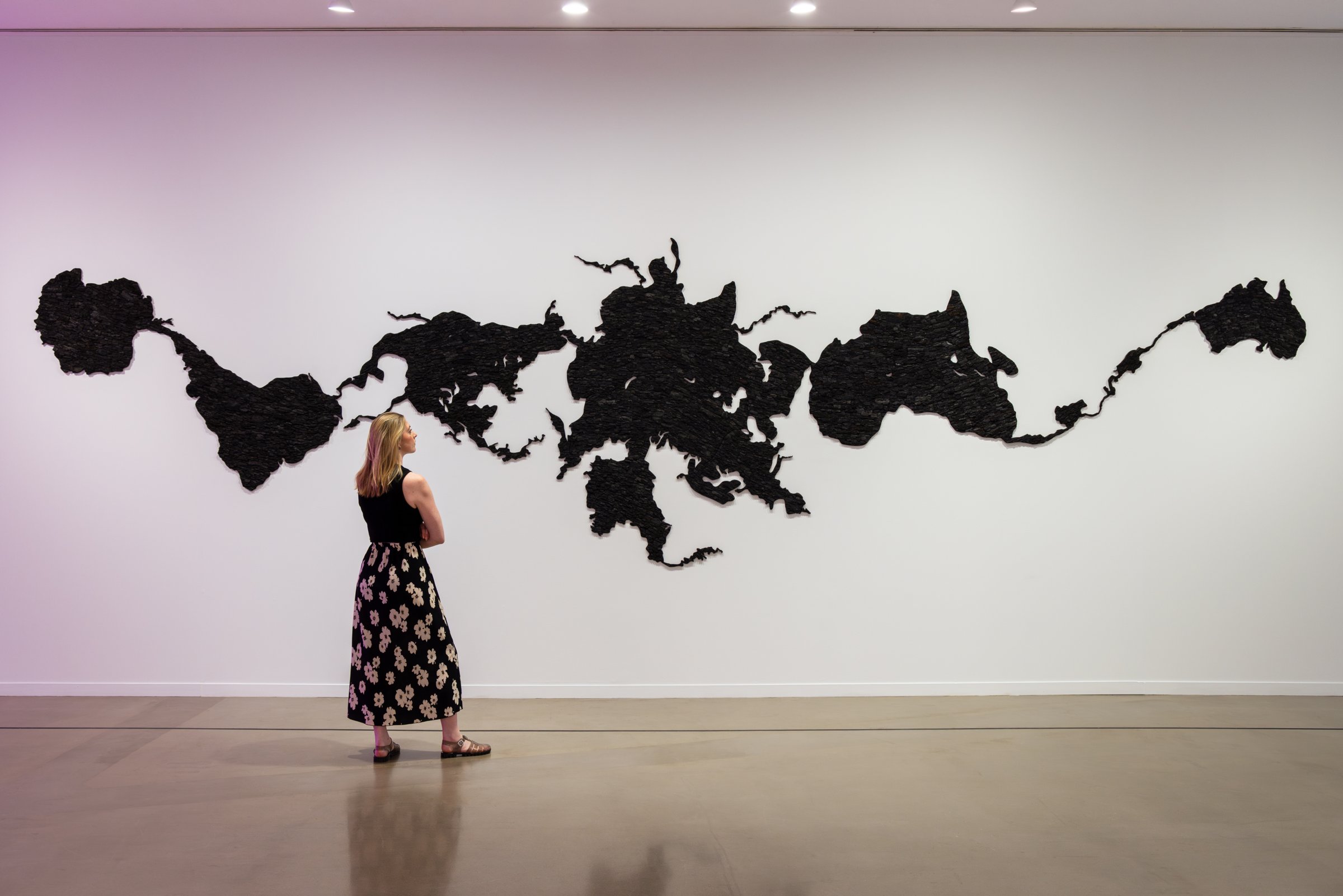 A visitor stands before Teresita Fernández’s black wall installation Island Universe, 2023