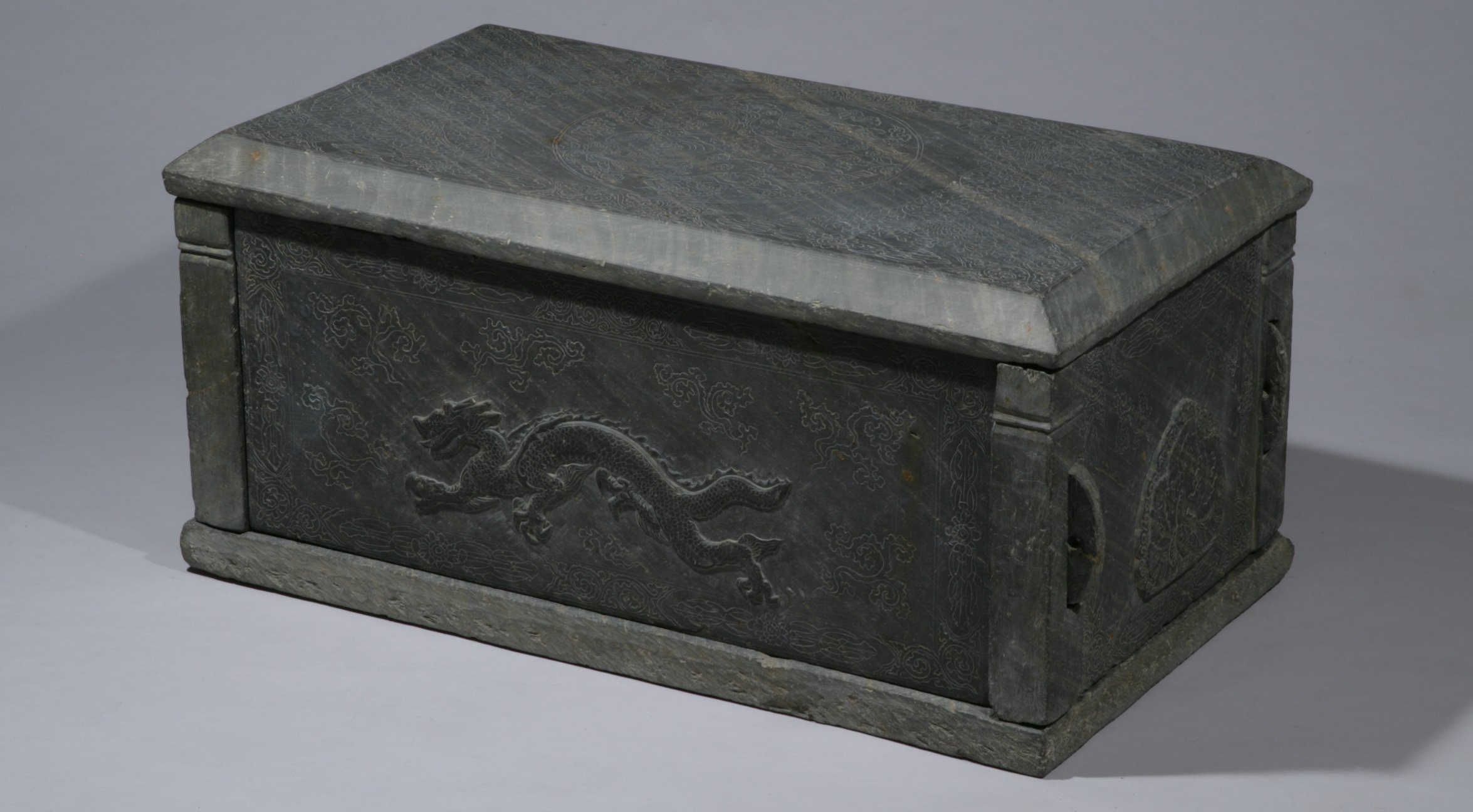 Dark stone coffin with a pitched lid and a dragon carved on its side
