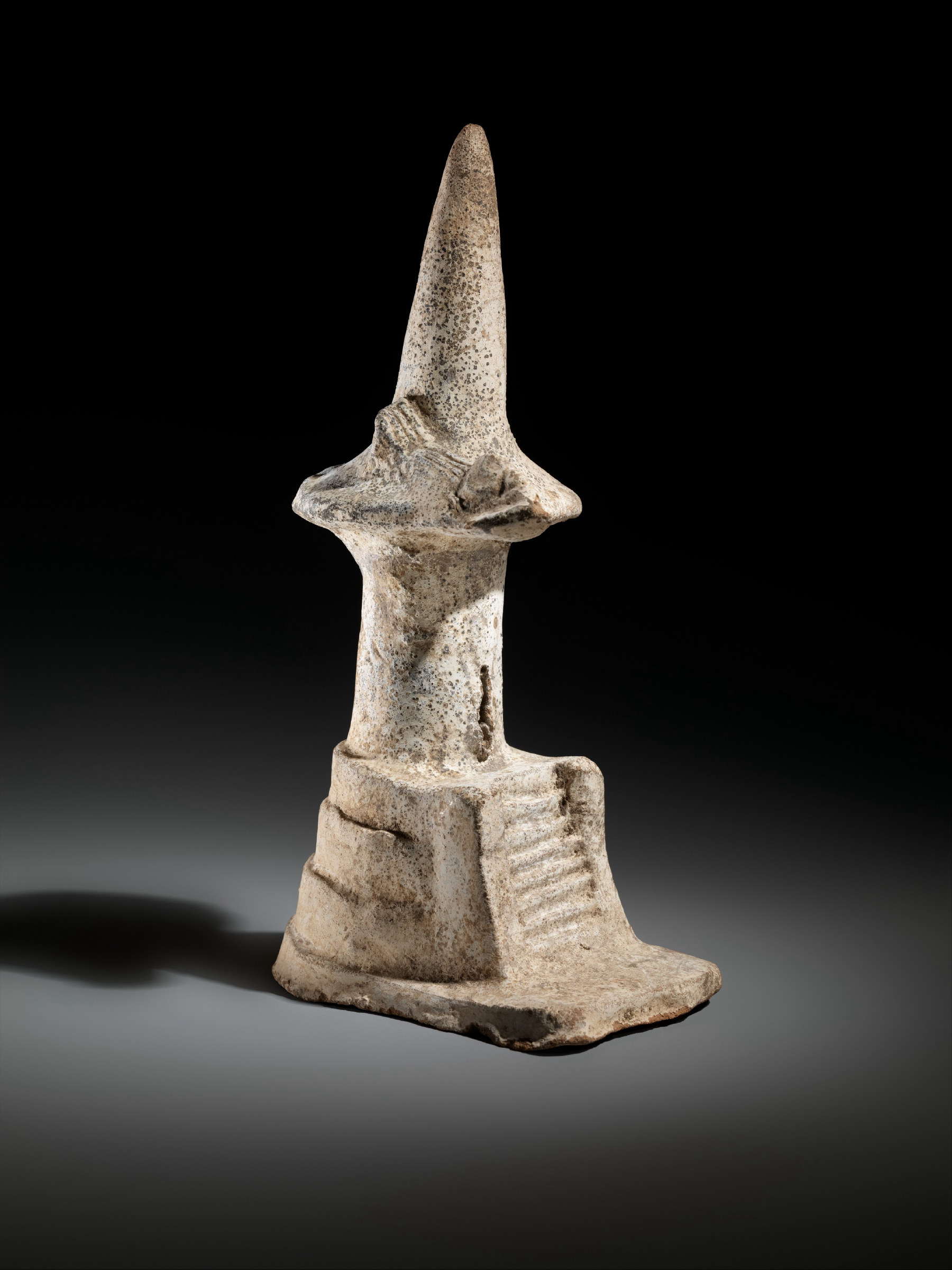 A small carved stone model of a temple: a tall conical roof rising from a rectangular shrine set on a low stepped platform.