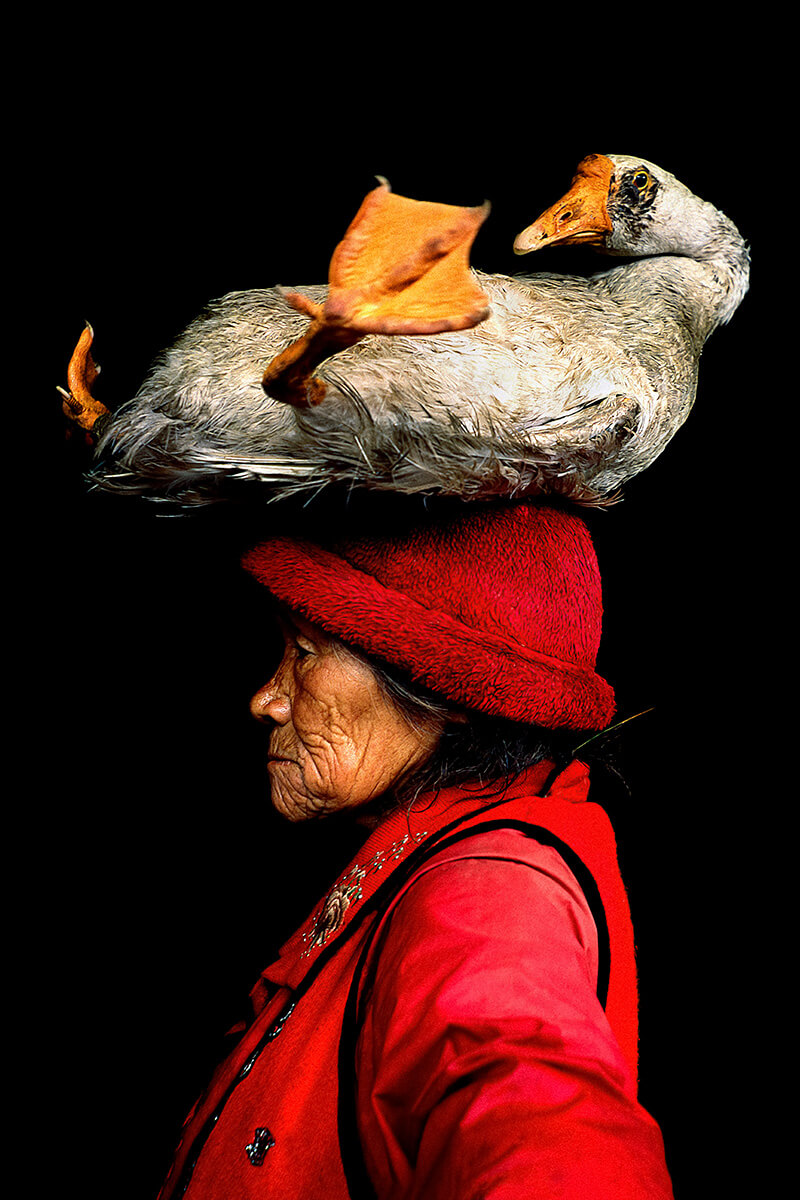Cristina Mittermeier, Lady with the Goose, 2008: a woman in a red hat and coat with a goose resting on her head