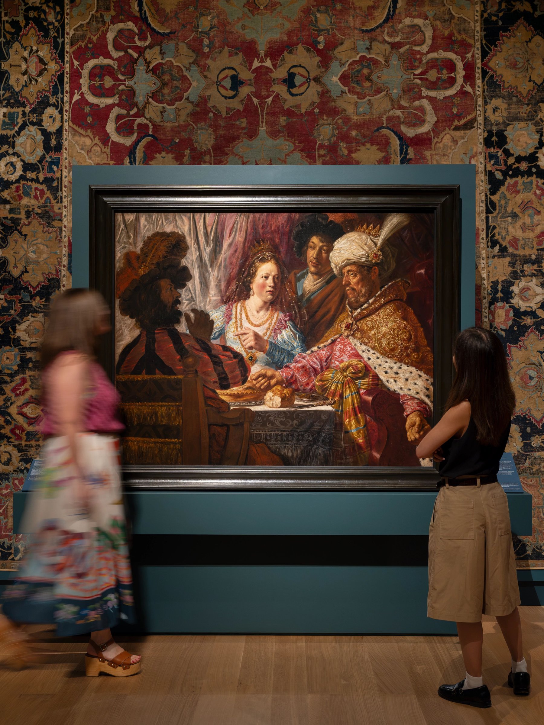 Visitors looking at a framed banquet painting in a teal gallery