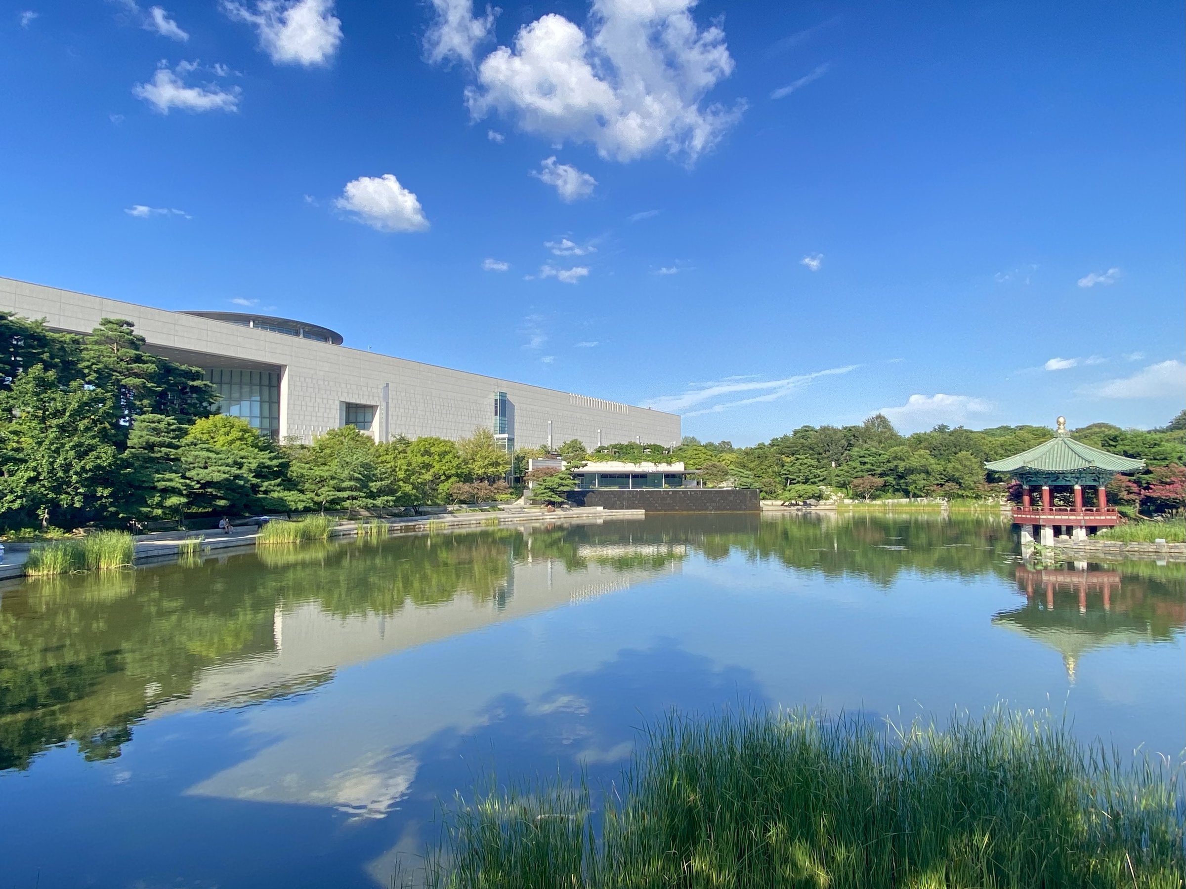 National Museum of Korea by day across the Mirror Pond, with a red pavilion, trees and blue sky