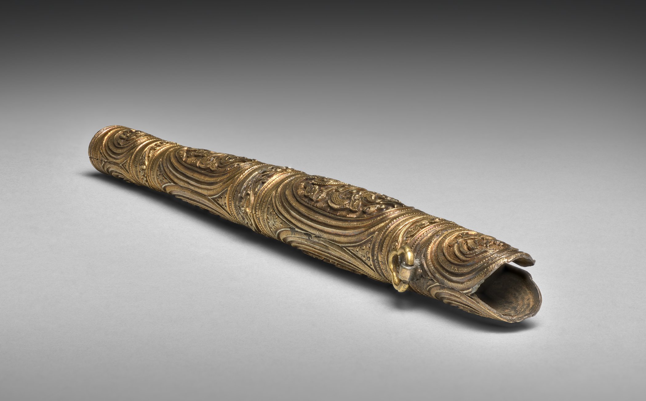 Gilt silver knife sheath with raised scrolling decoration, lying on its side