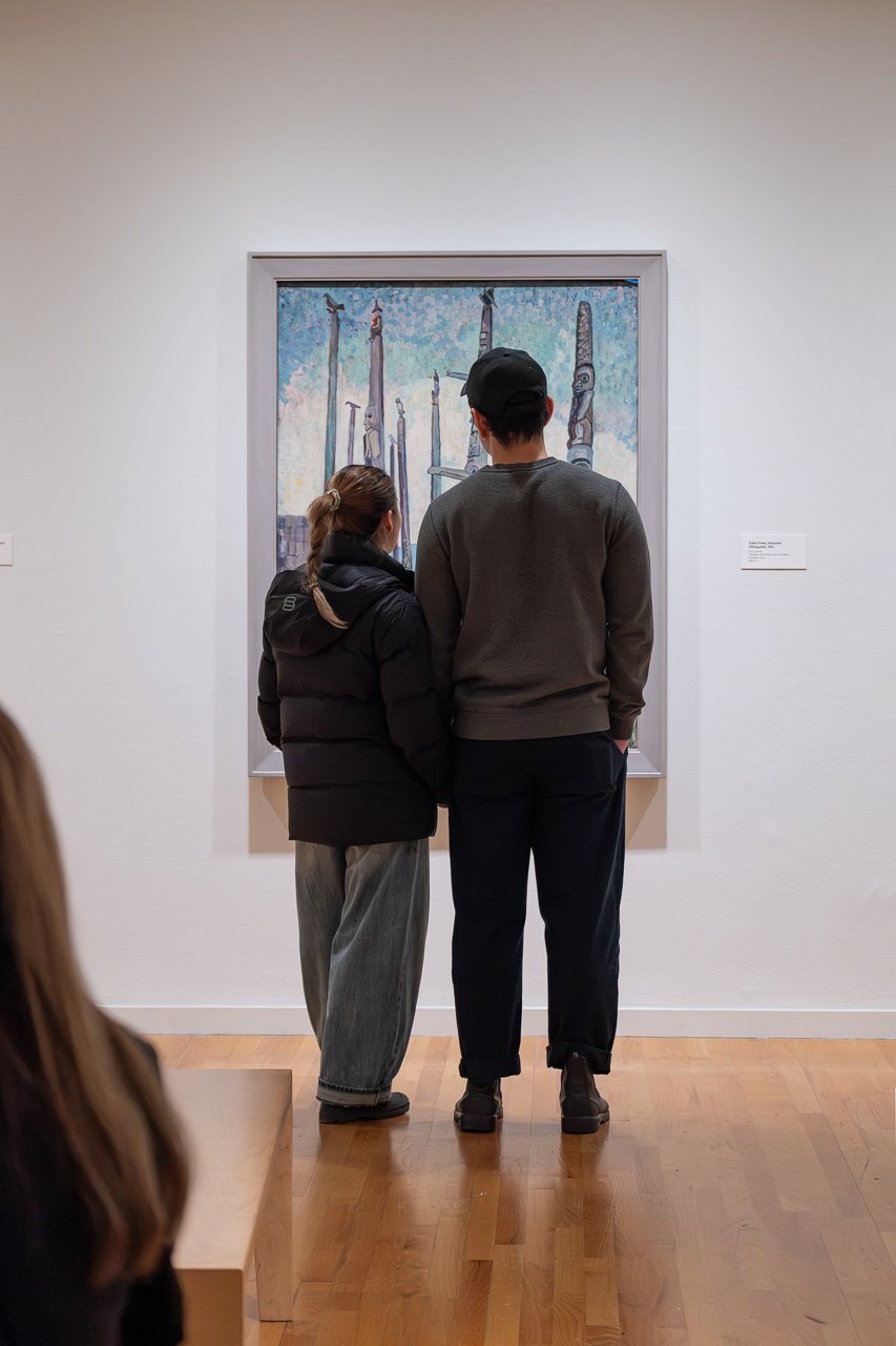 Two visitors view an Emily Carr painting of tall trees at Free First Friday
