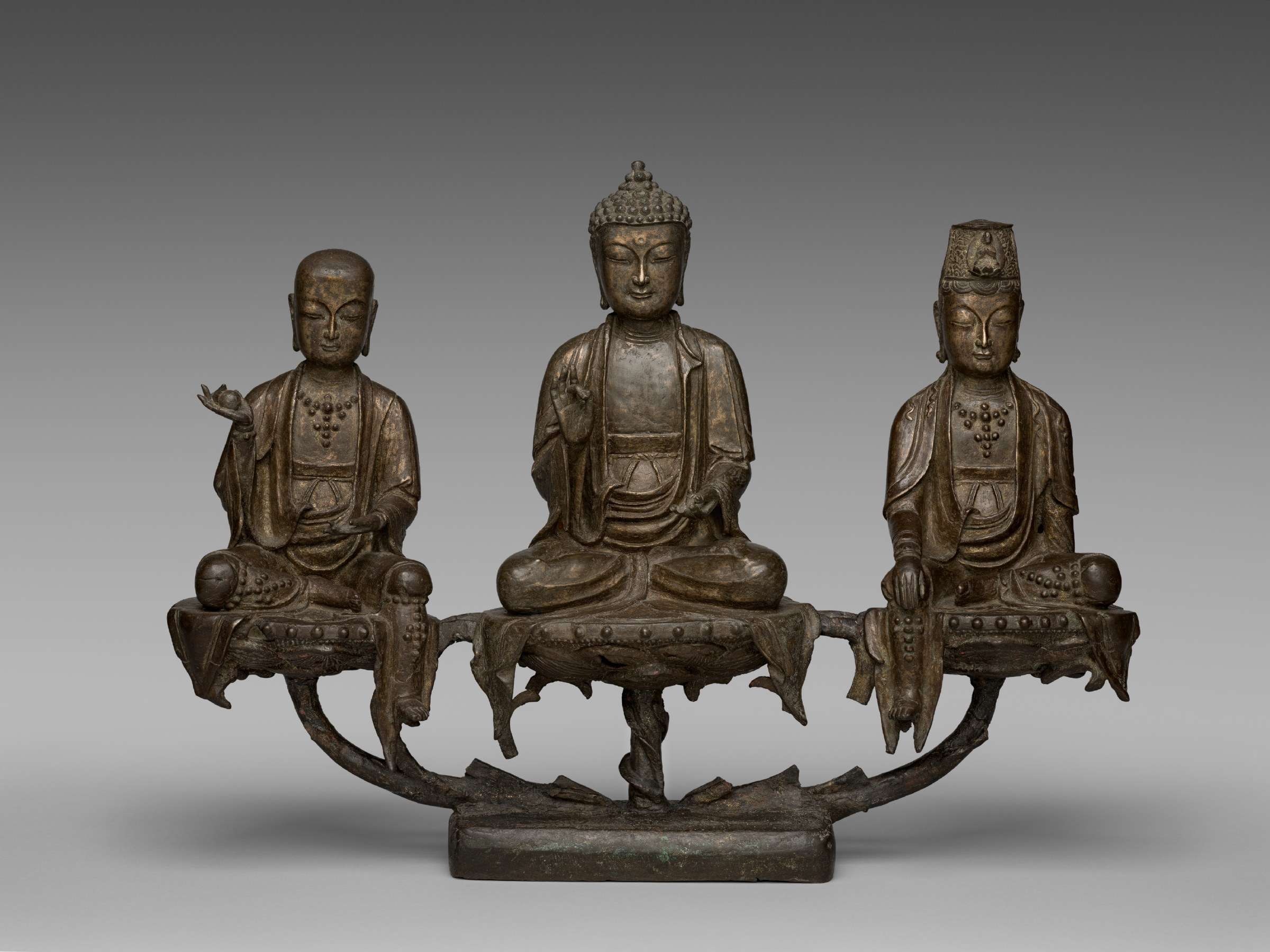 A small gilt-bronze shrine group: the Amitabha Buddha seated on a lotus throne at the centre with a standing-haloed bodhisattva on either side, all three mounted on a single base.