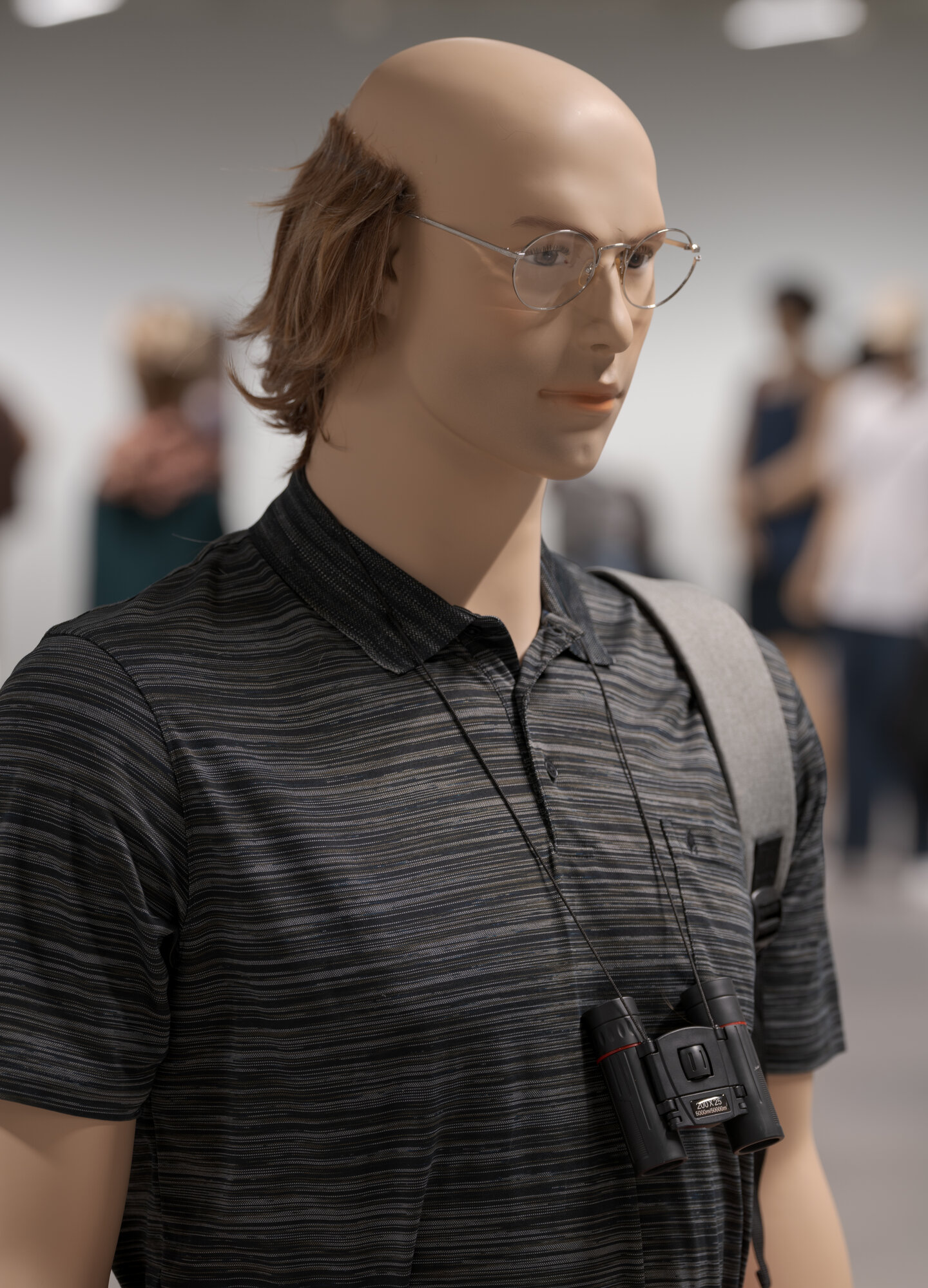 Installation view of "The Populace" at ARoS, a bald mannequin figure wearing a camera and lanyard