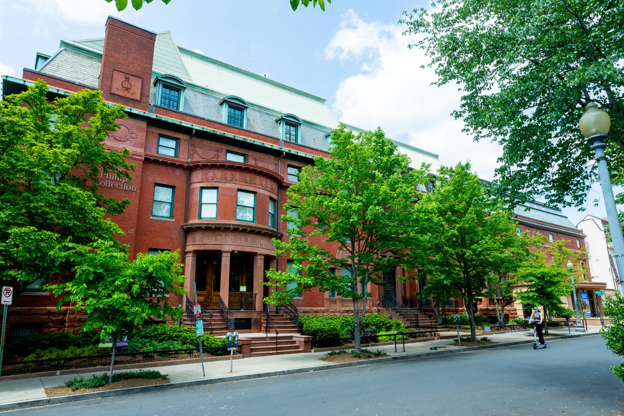 The Phillips Collection's original red brick and brownstone house on 21st Street NW, Washington, seen at an angle behind summer street trees