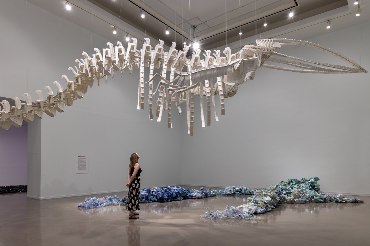 A visitor stands beneath a suspended whale skeleton sculpture in Future Geographies at the Vancouver Art Gallery