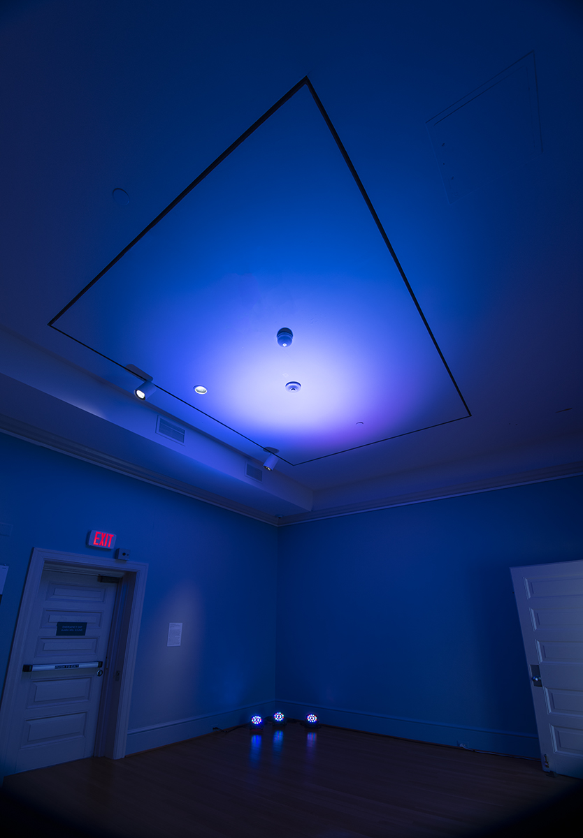 Gallery bathed in blue light with a suspended triangular frame overhead
