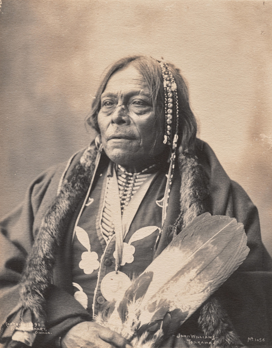 Frank A. Rinehart, John Williams – Tonkawa: a seated portrait of a Tonkawa man with hair ornaments, holding a feather fan