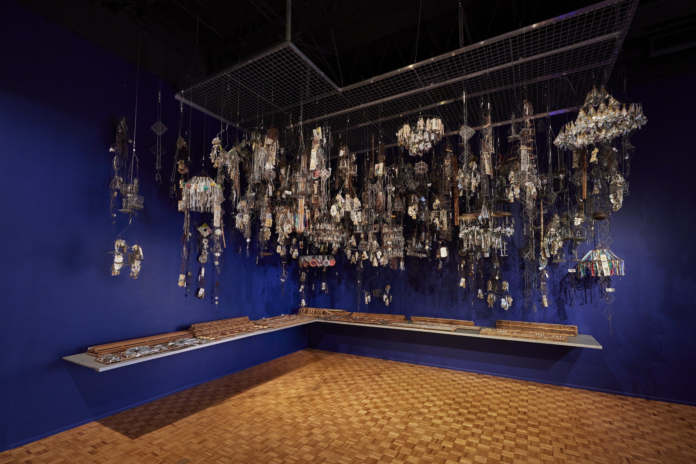 Emery Blagdon’s Healing Machine, many hanging metal components suspended in a dark blue gallery