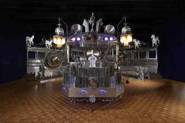 Guadalupe Maravilla sculptural sound altar crowned with figures and lights in a dark gallery with a wood floor