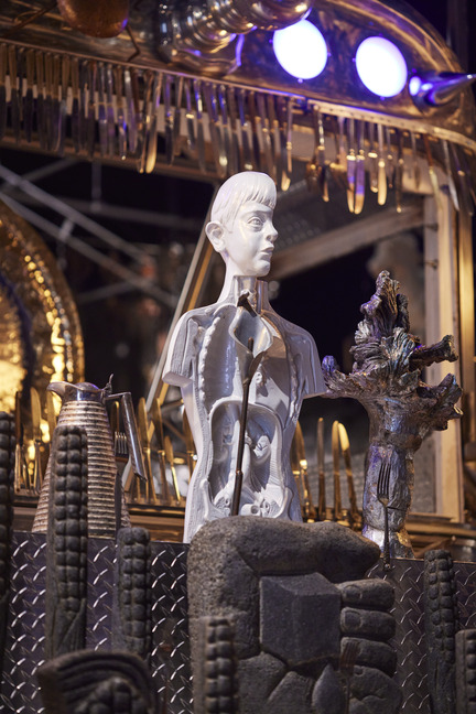 Detail of a pale sculpted figure on a tall carved column lit by stage lights