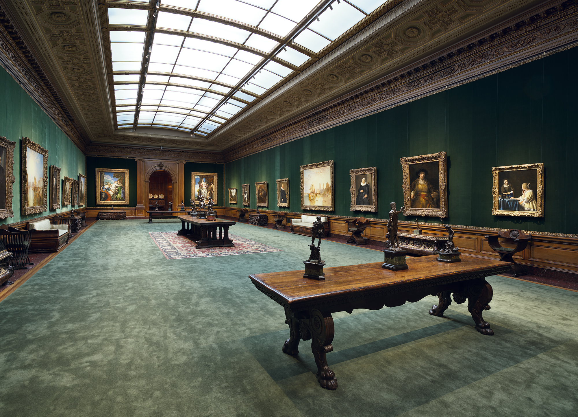 The West Gallery: a long skylit gallery with green walls hung with paintings, a carved table and bronze sculptures down the centre.