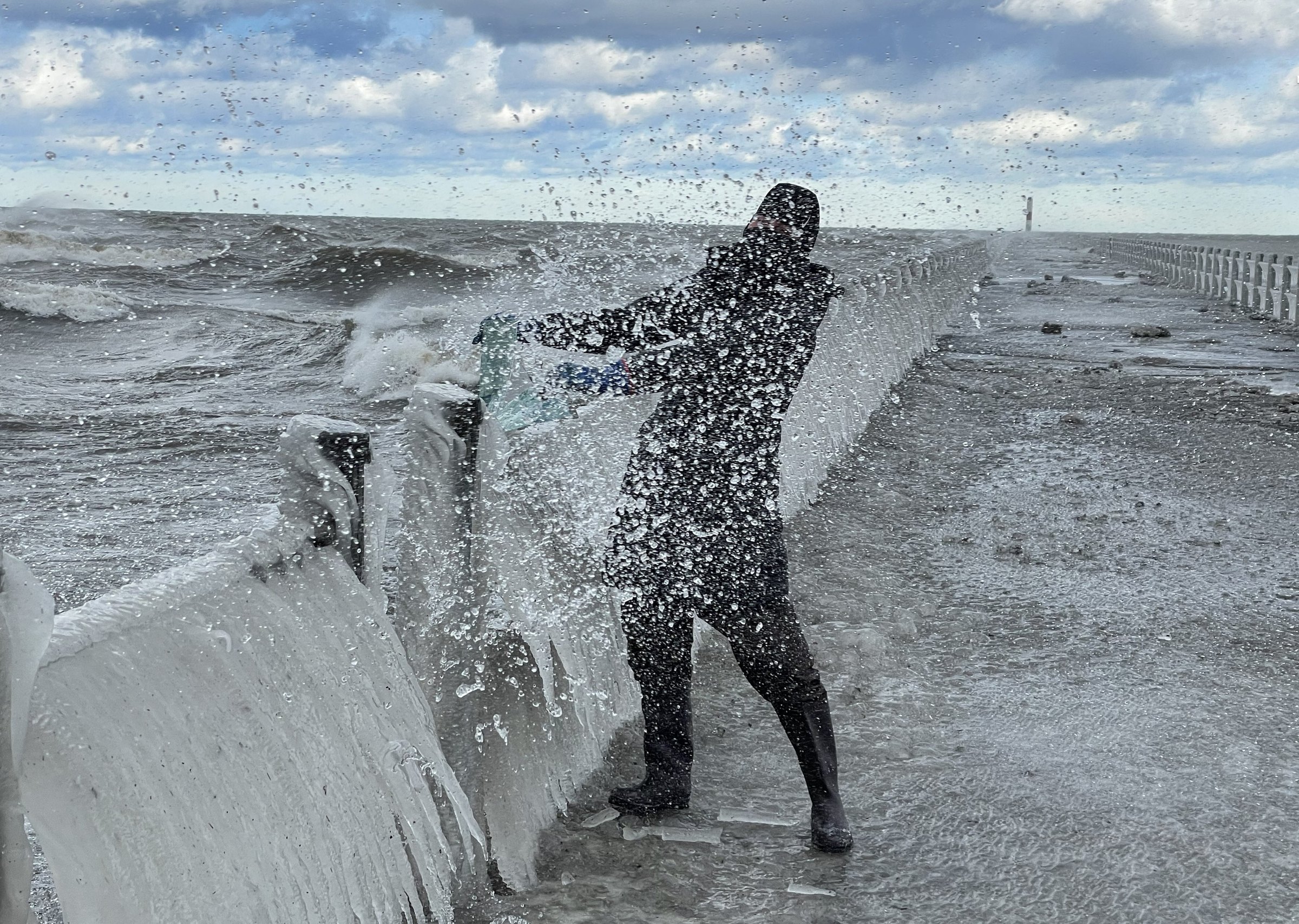 Meghann Riepenhoff holding a large sheet as a wave splashes over her at the shore