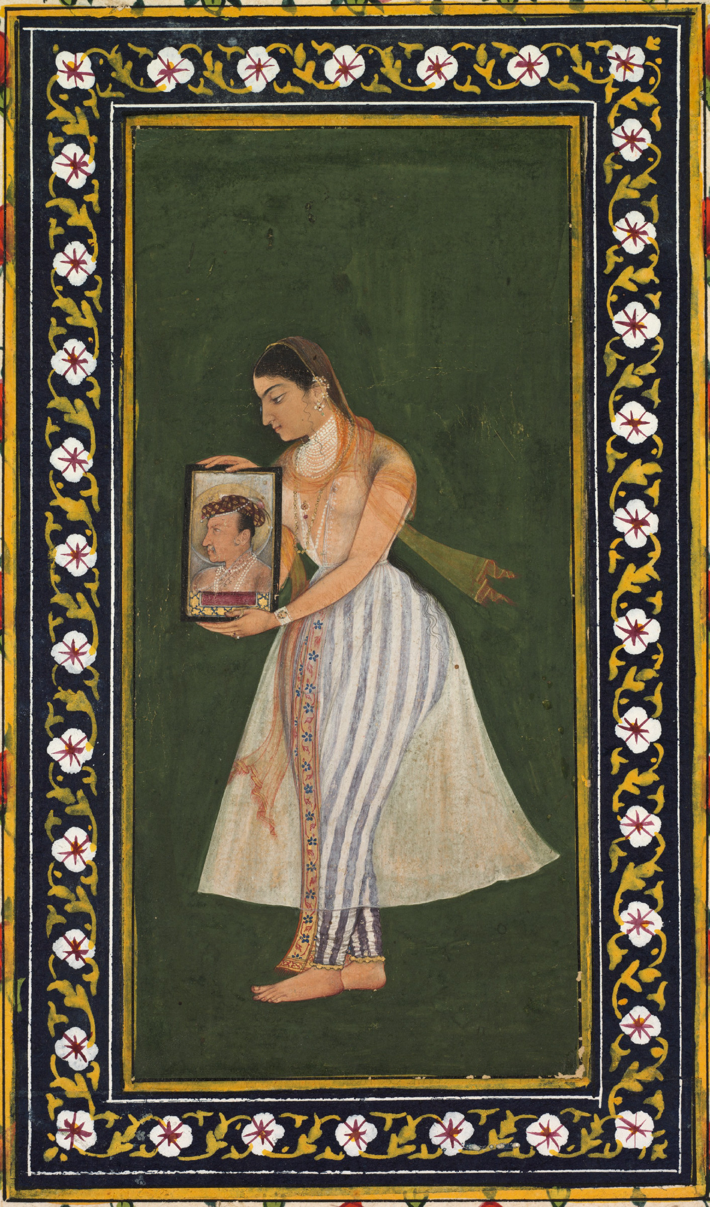 A Mughal miniature within an ornate floral border: the empress Nur Jahan stands in profile against a plain green ground, wearing a striped skirt and a translucent veil, holding a small framed portrait up before her.