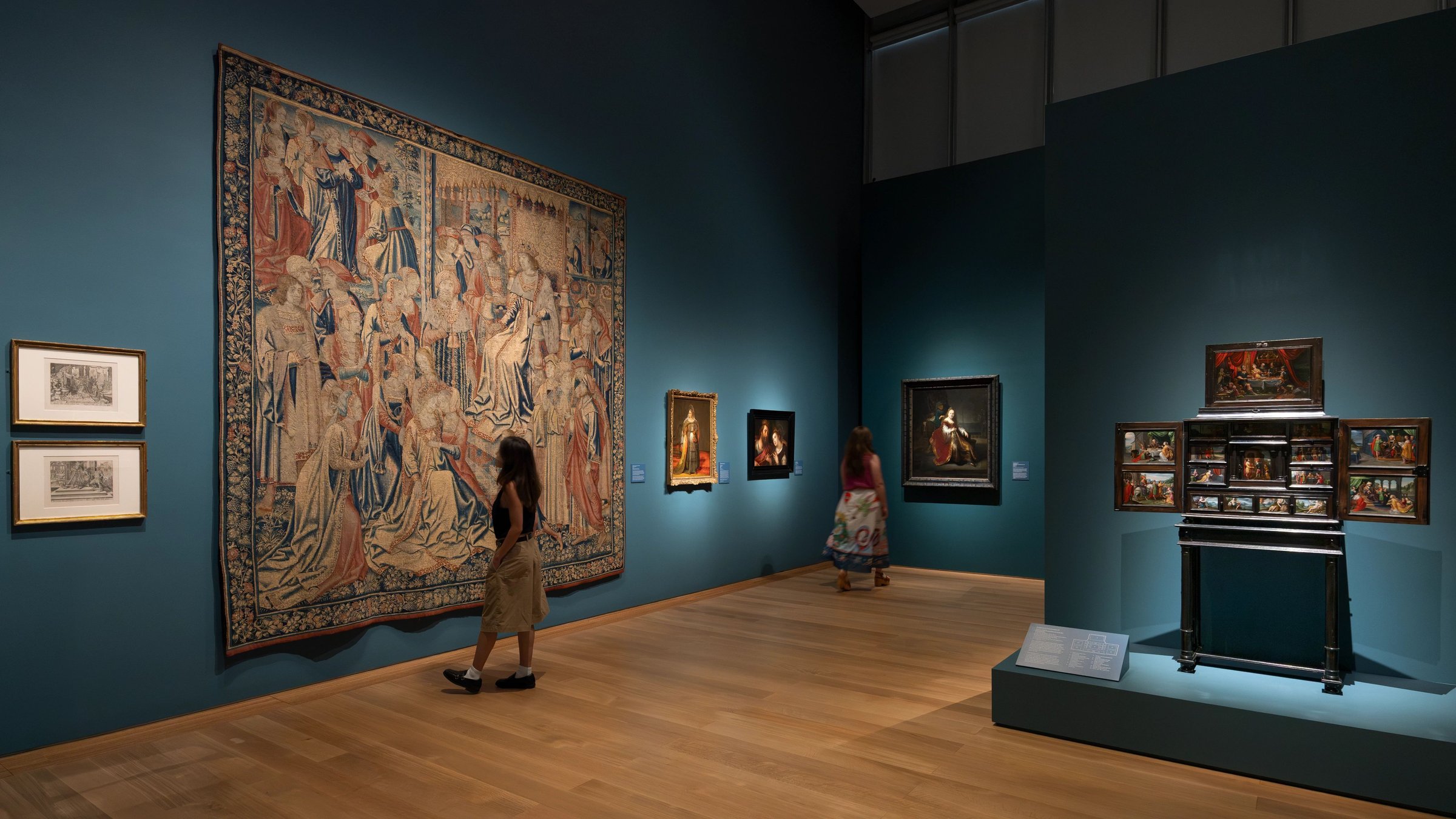 Gallery with a large Flemish tapestry, paintings and a display case in a deep teal room