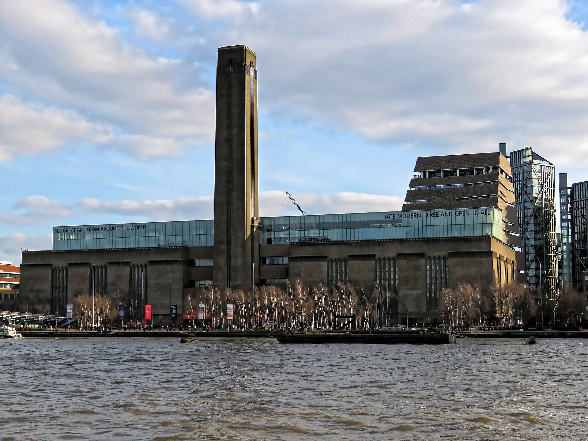 Tate Modern seen from across the Thames: the long brick mass of the former Bankside Power Station with its tall square chimney, the glass Blavatnik extension rising behind.