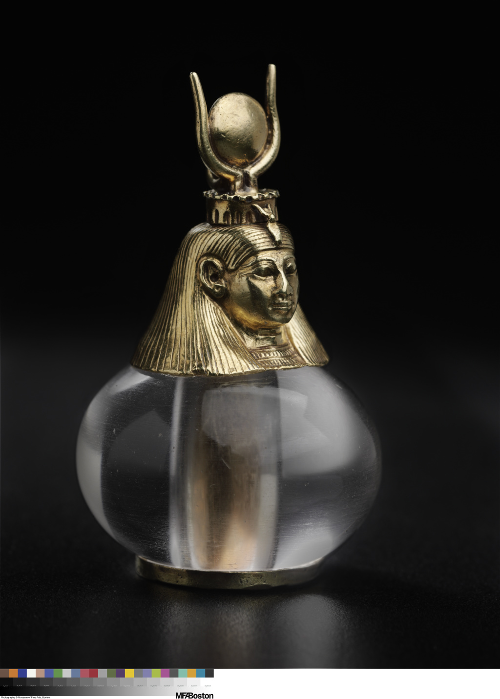 Pendant of a gold head topped with an elaborate headdress attached to a clear, somewhat flattened sphere.