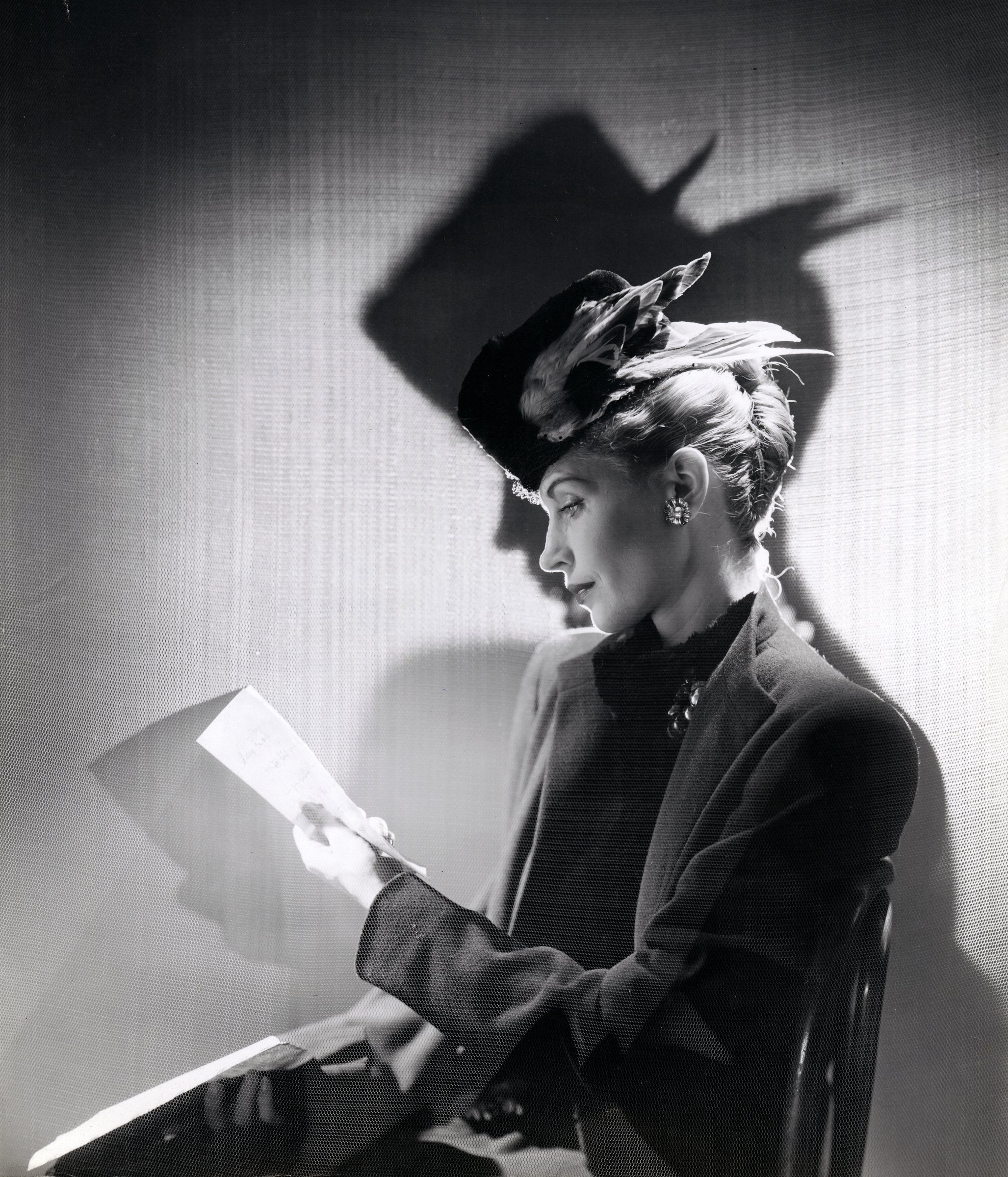 Cecil Beaton, Fashions Made to Order: a woman in a wool coat and feathered hat reading a letter, in dramatic light
