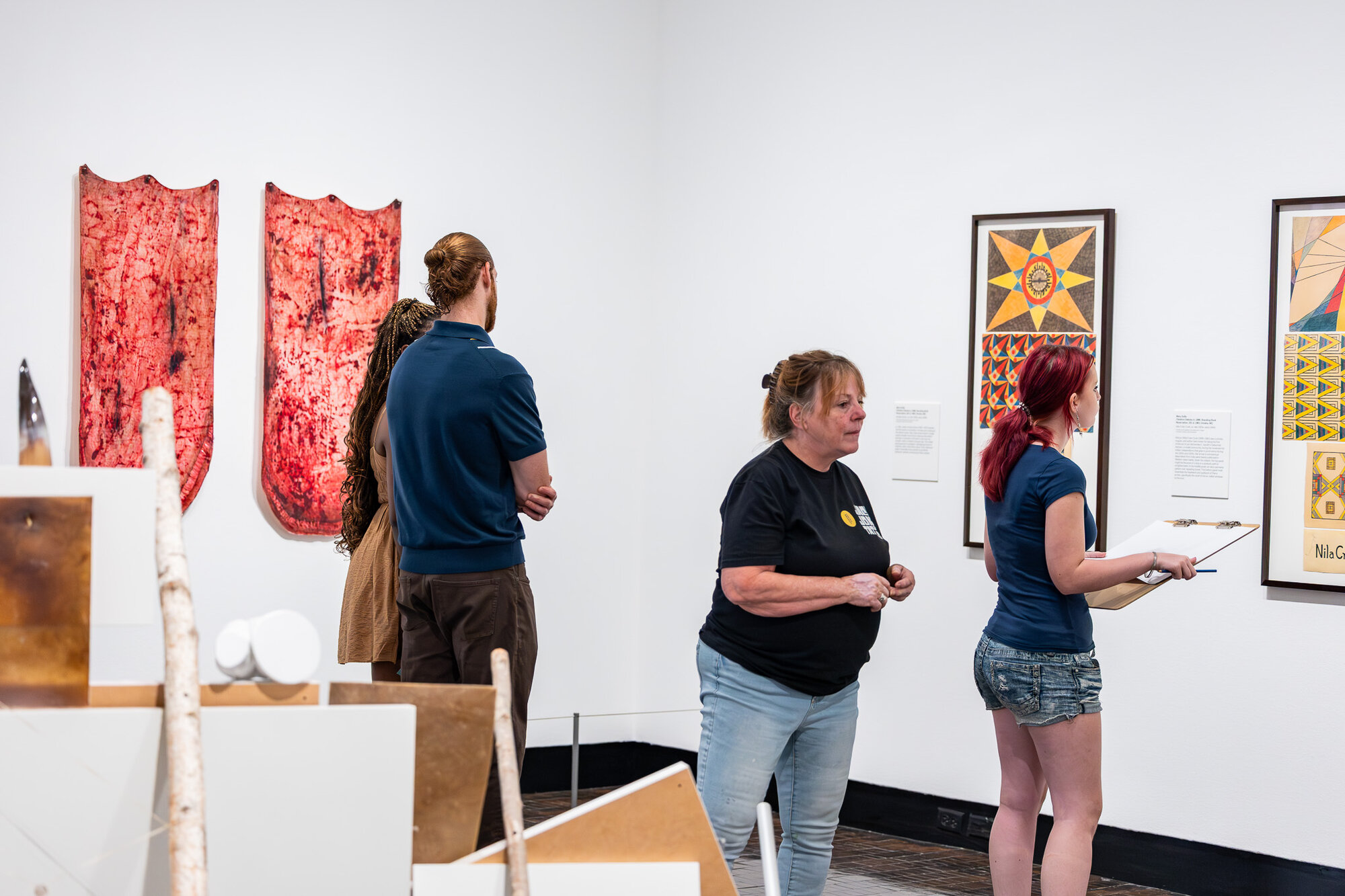 Visitors and a docent viewing textile and sculptural works in "An Indigenous Present" at the Frist Art Museum