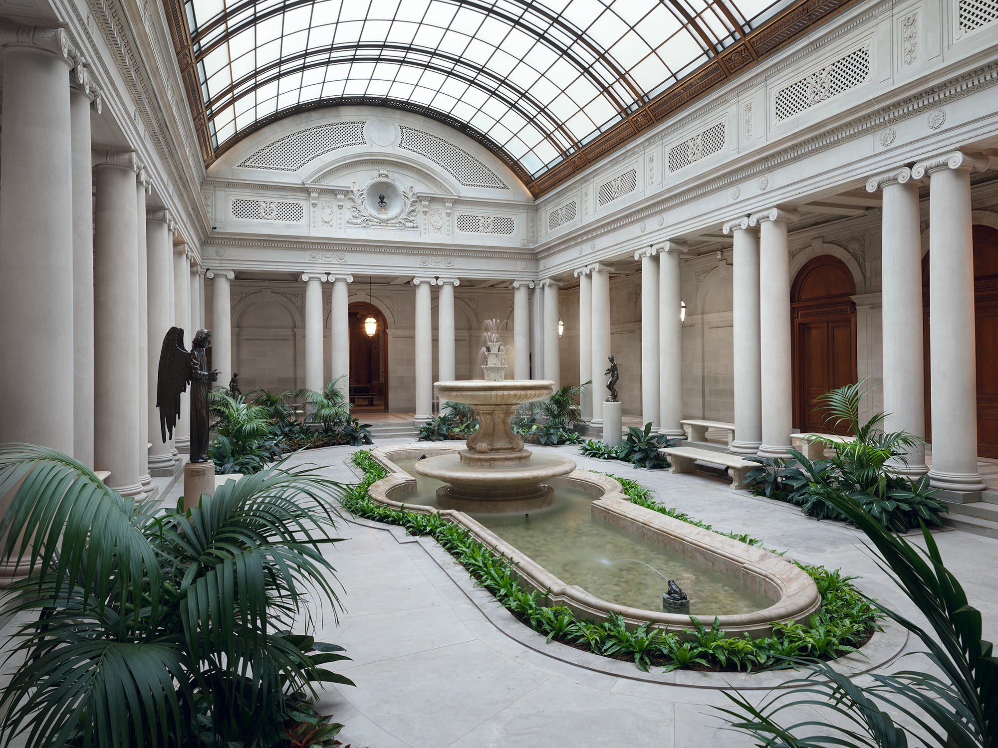 The Garden Court: a skylit marble courtyard with paired columns, a central fountain and pool, and tropical plantings.