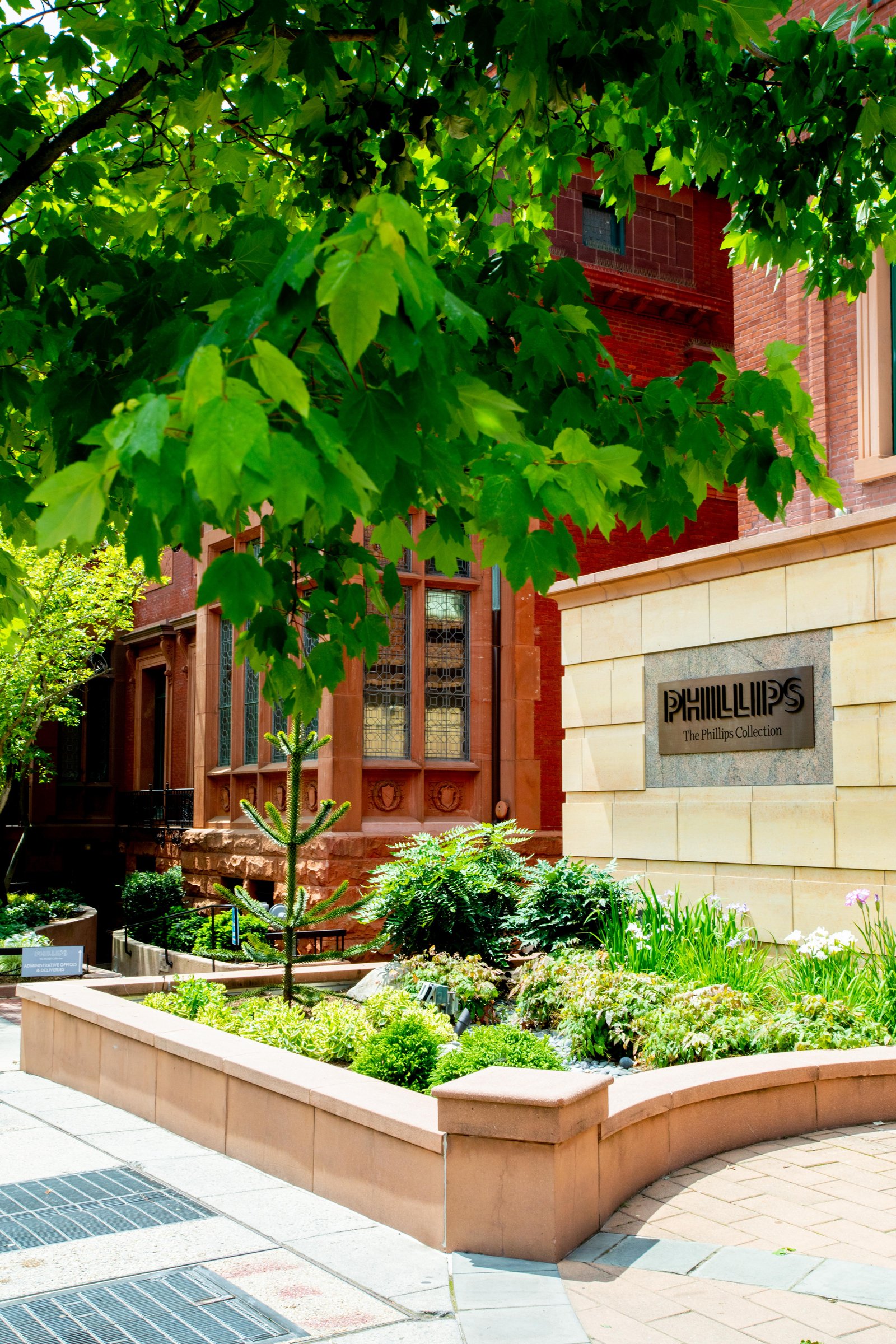 The Phillips Collection entrance with its name carved in stone, framed by green trees and planters