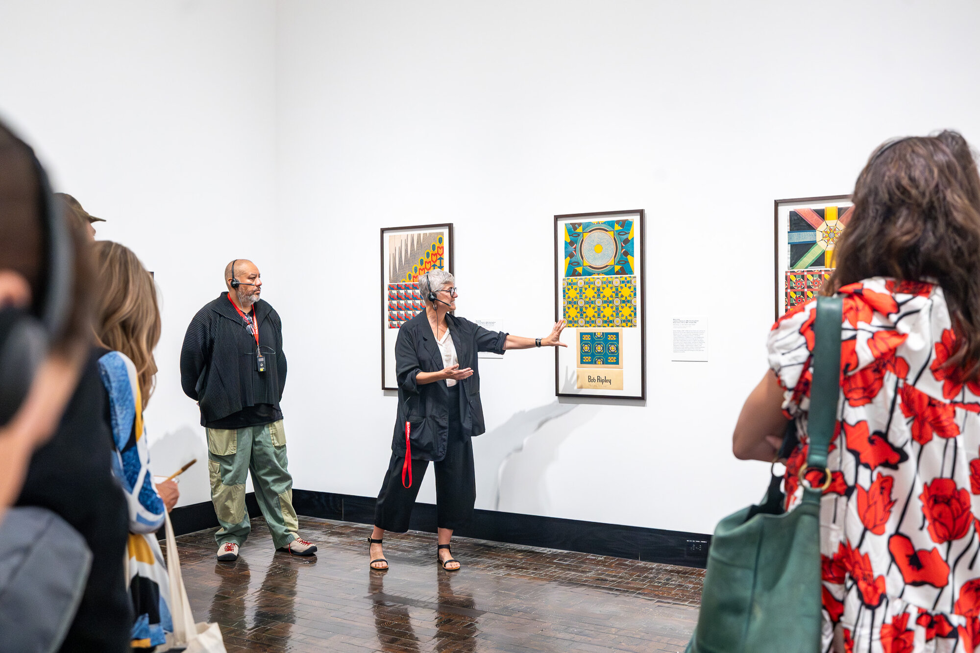 A docent speaking with visitors in front of framed paintings in "An Indigenous Present" at the Frist Art Museum