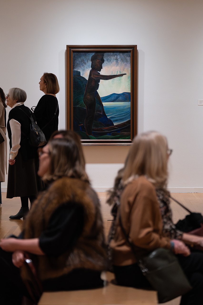 Visitors seated before an Emily Carr painting of a tree by the sea